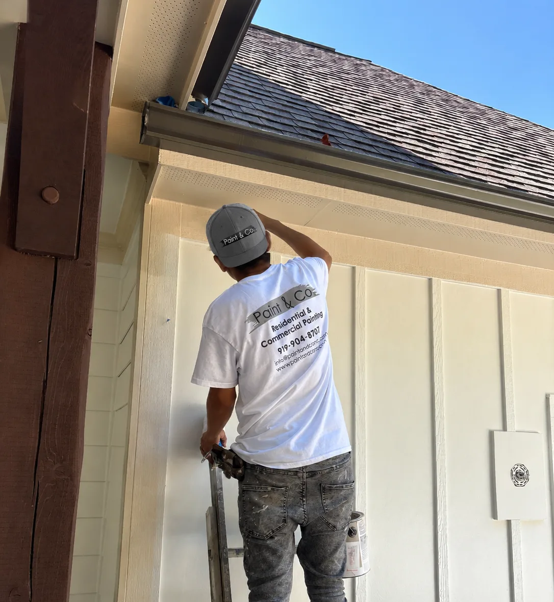 Painter on a ladder painting white board-and-batten siding under the roof eaves