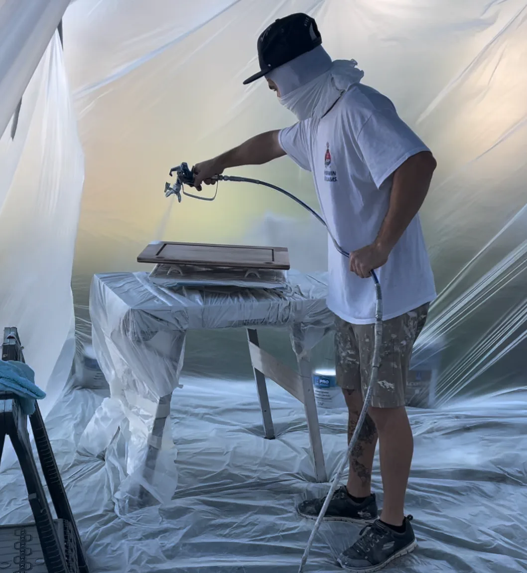 Painter spraying cabinet doors inside a plastic-lined spray booth