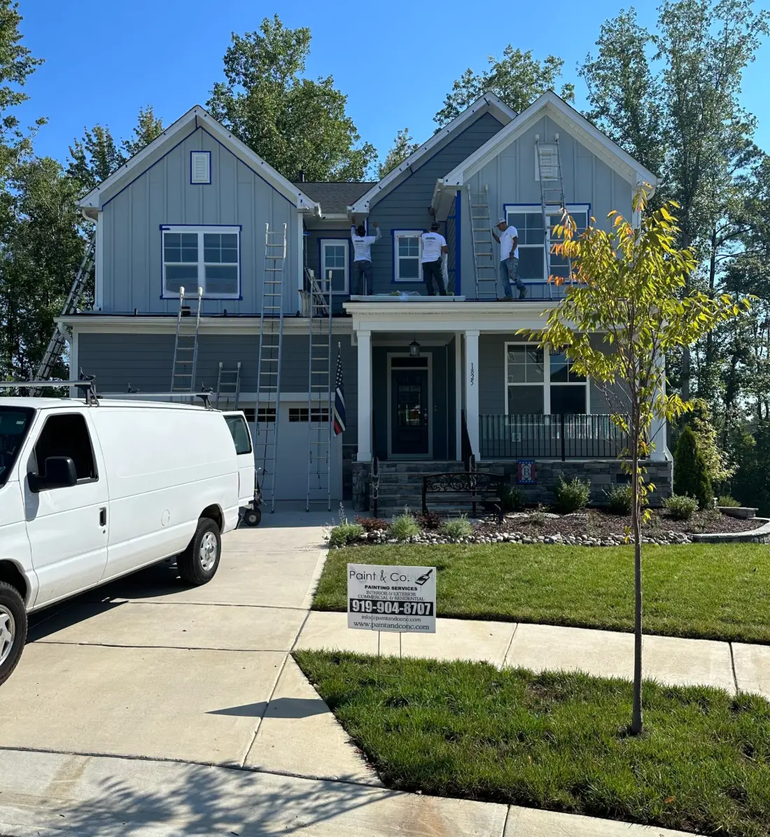 Painting crew working on a two-story home with the company van and yard sign out front